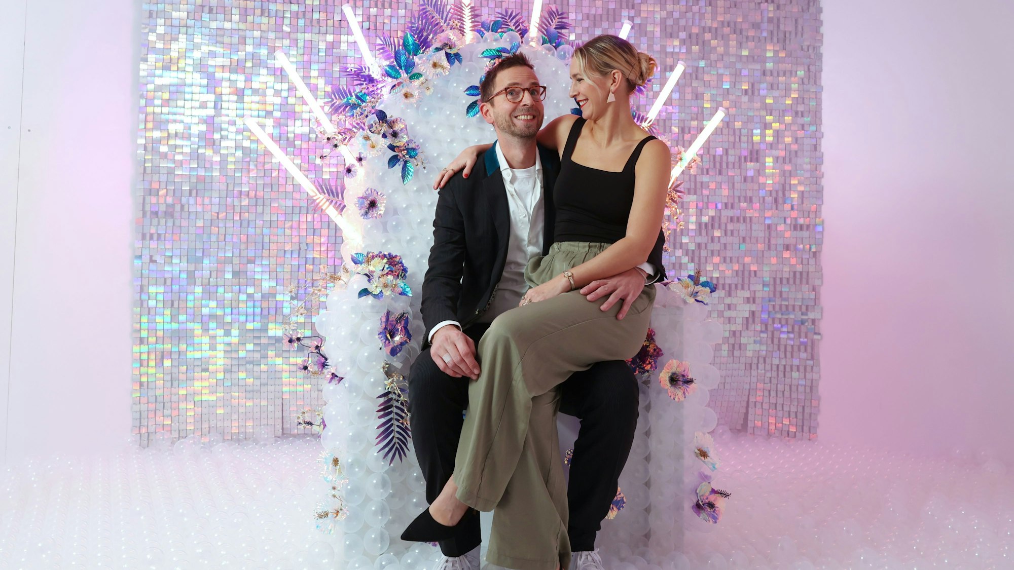 Selina Weiershäuser und Nico Zingelmann sitzen auf einem weißen Stuhl mit Blumen und durchsichtigen Bällen.