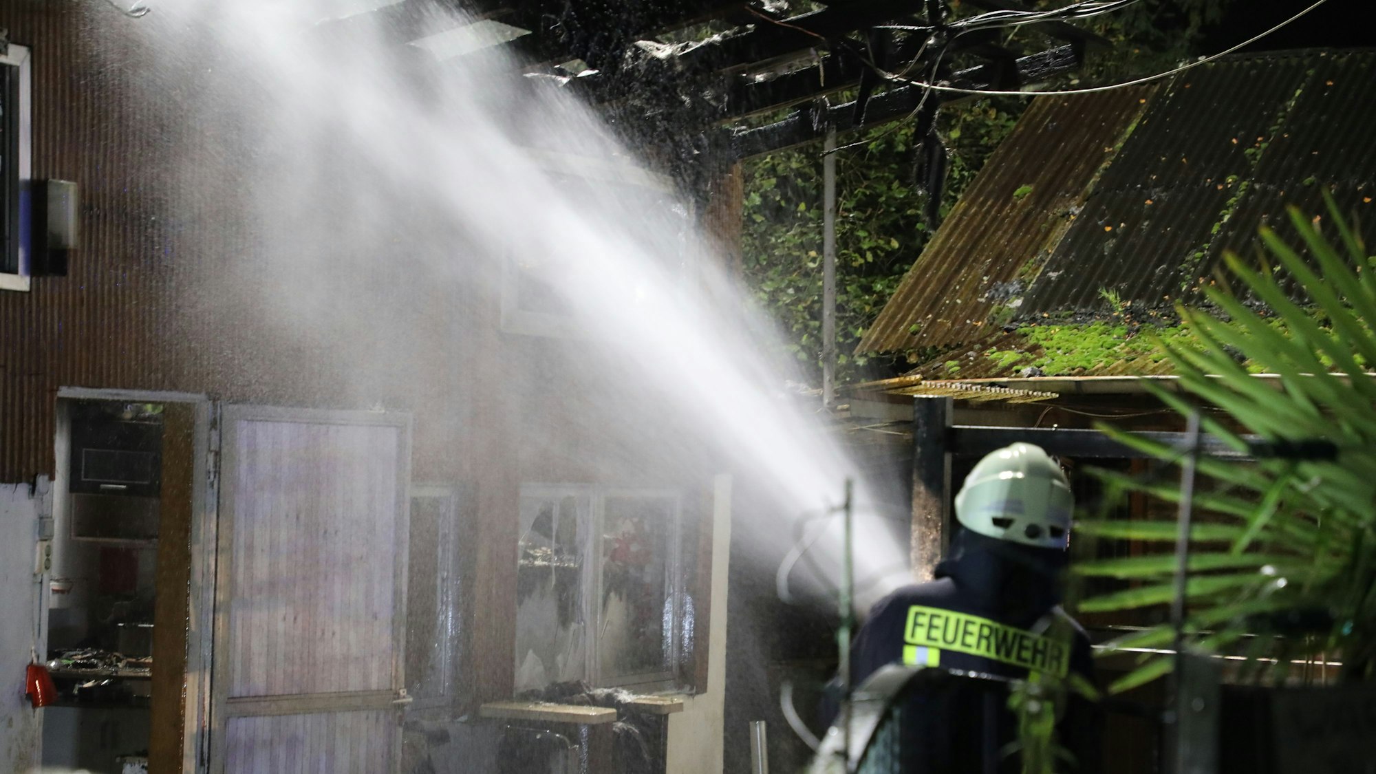Ein Feuerwehrmann löscht einen Brand in einem Holzgebäude.