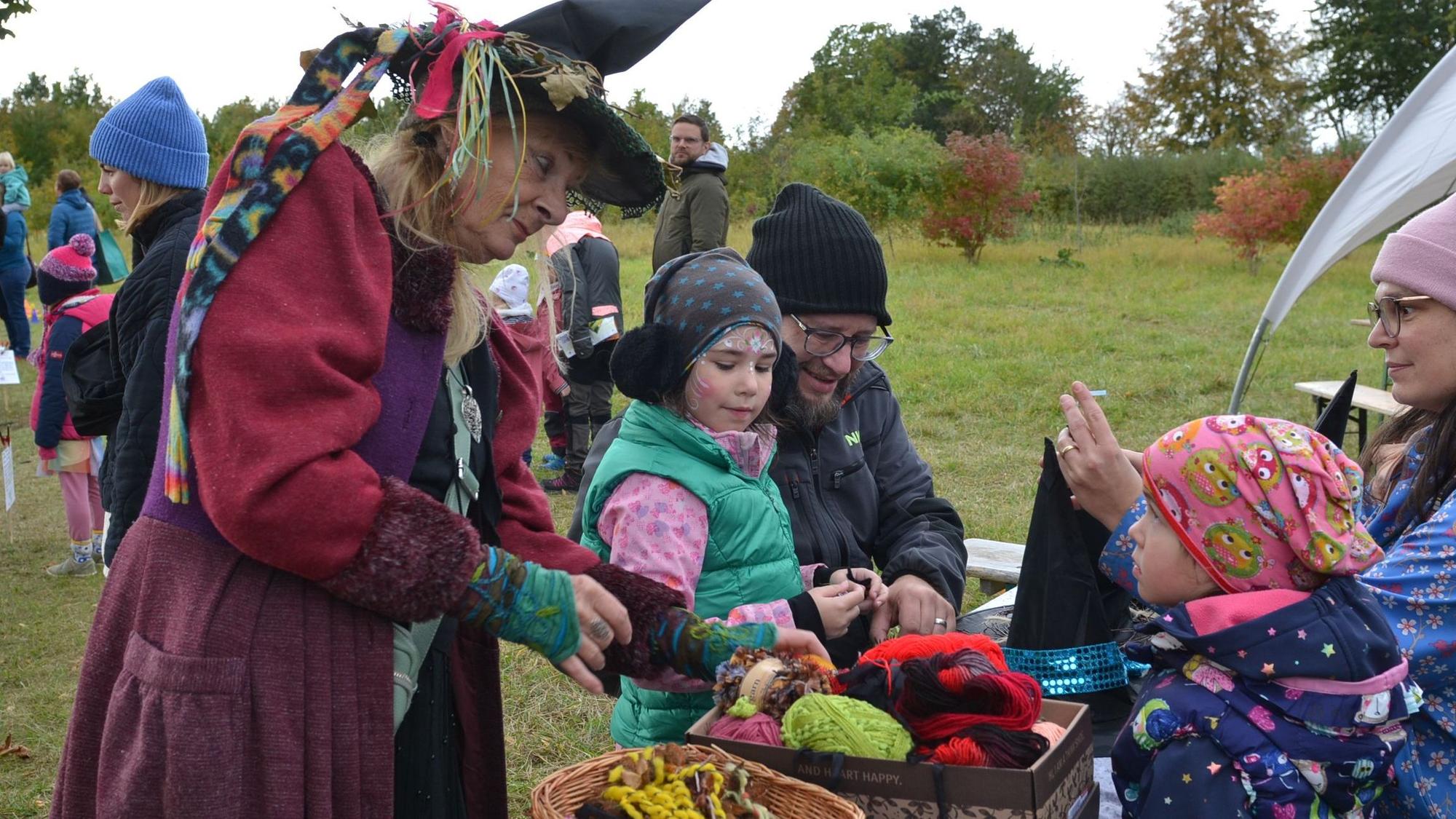 Eine als Hexe verkleidete Frau bastelt mit zwei Kindern und deren Eltern Hexenhüte.