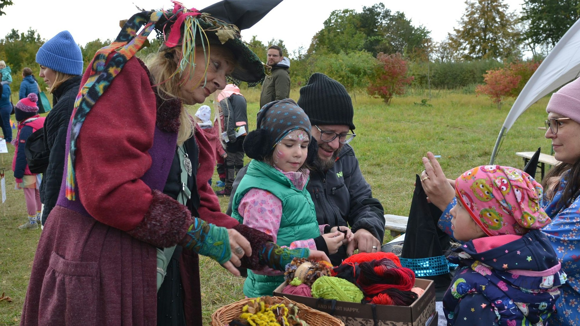 Eine als Hexe verkleidete Frau bastelt mit zwei Kindern und deren Eltern Hexenhüte.