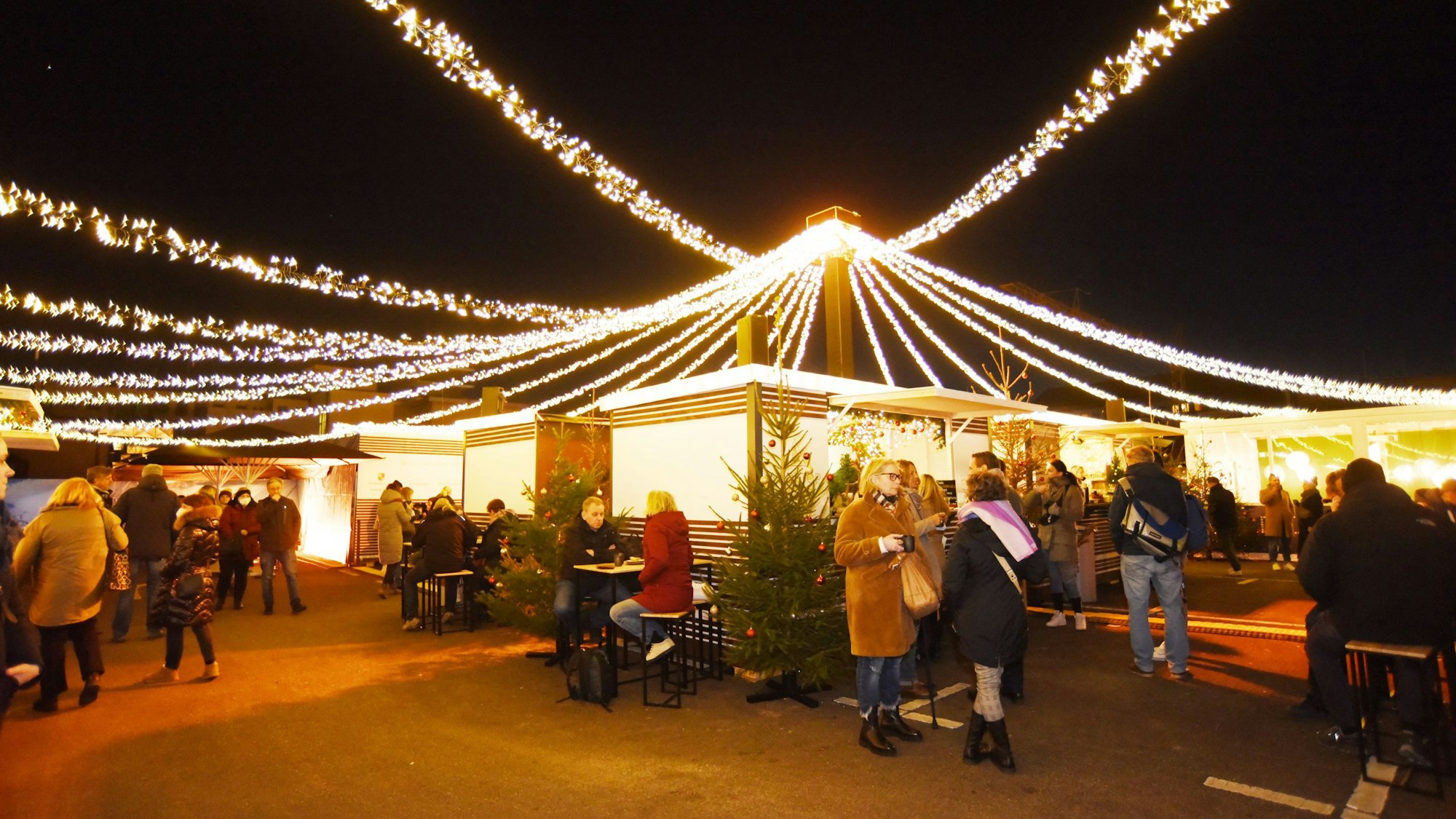 Menschen stehen vor Weihnachstmarktbuden, über ihnen ziehen sich Lichterketten.