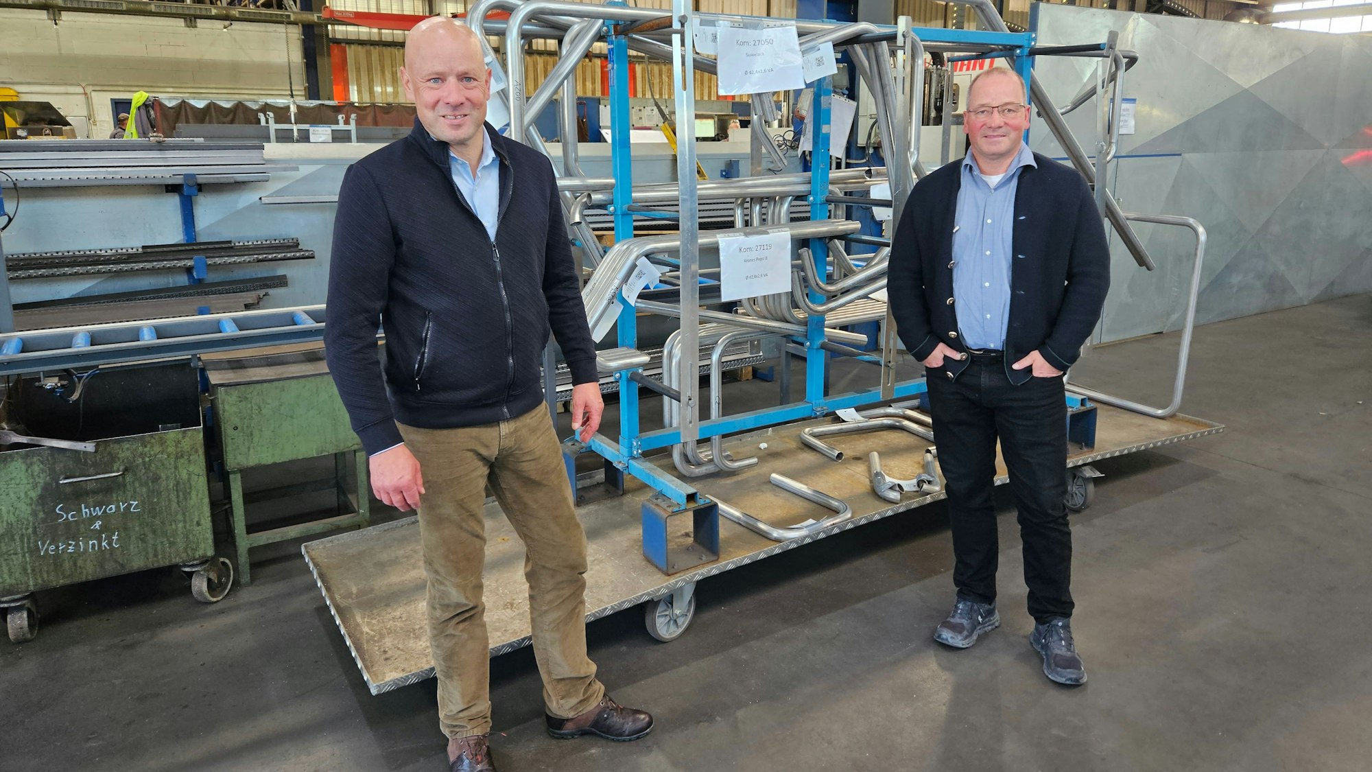 Thomas und Josef Müller (r.) stehen vor Stahlbauteilen in einer Werkshalle.