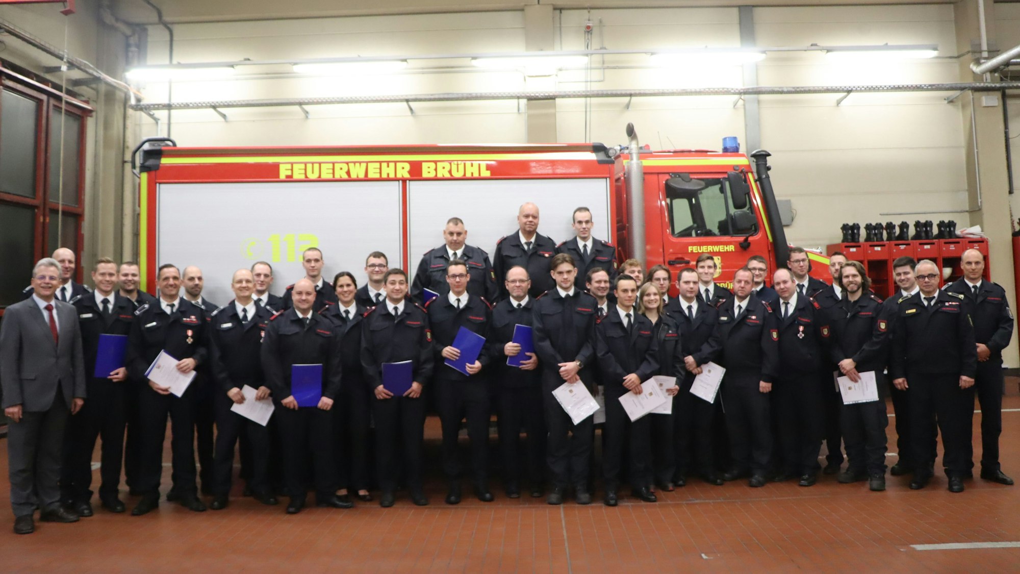 Auf dem Foto sind Mitglieder der Freiwilligen Feuerwehr aus Brühl zu sehen. Sie stehen vor einem Löschfahrzeug. Einige von ihnen halten Urkunden in der Hand.
