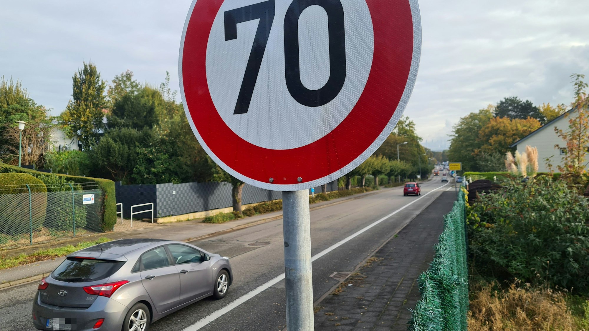 Auf dem Foto ist die Sankt-Rochus-Straße in Bedburg-Kaster zu sehen. Ein grauer Wagen passiert ein Tempo-30-Schild.