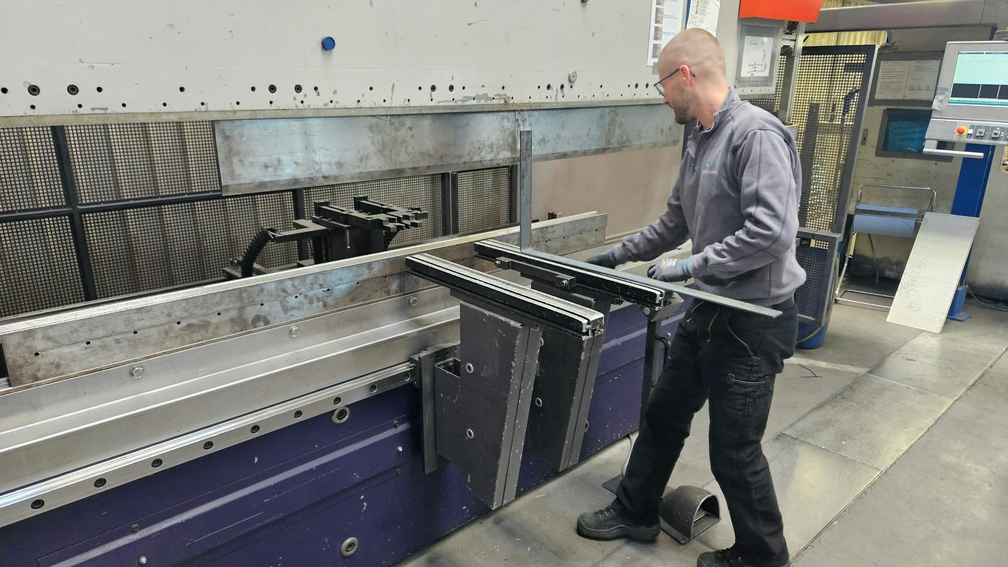 Zu sehen ist ein Mitarbeiter einer Stahlbaufirma, der Metall bearbeitet.