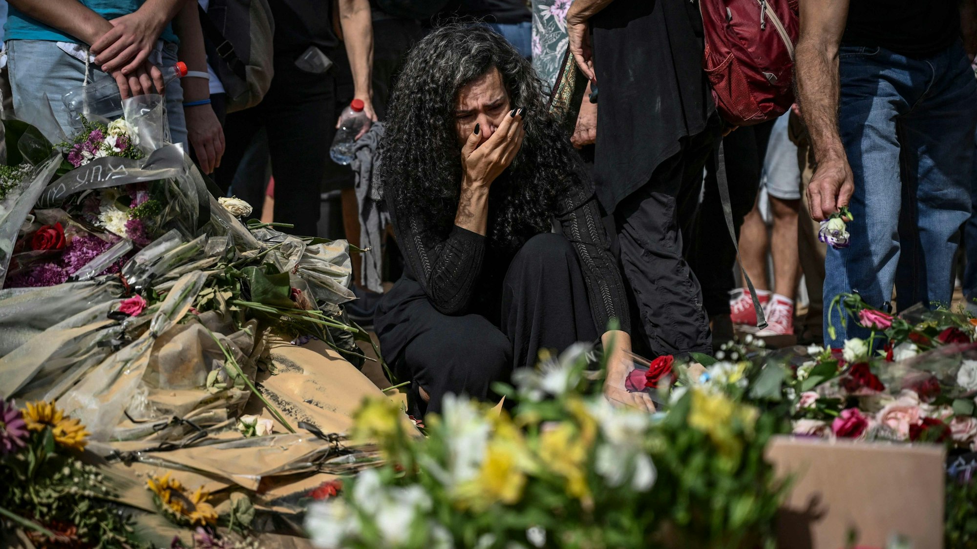 EIne Frau, umringt von Blumensträußen, trauert um David Carroll, der von der Hamas im Kibbuz Beeri umgebracht wurde.