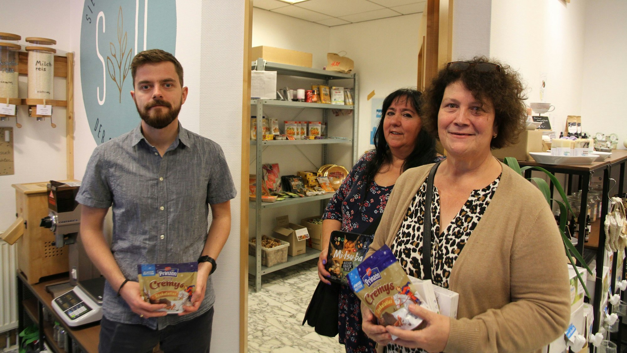 Ein Mann und zwei Frauen in einem Geschäft an der Siegburger Kaiserstraße halten Packungen mit Lebensmitteln in der Hand