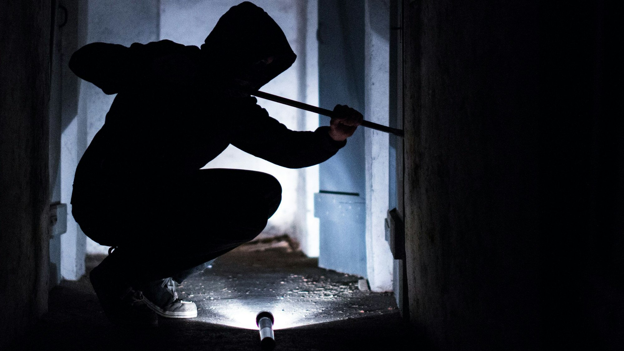 Ein Mann hebelt mit einem Brecheisen eine Tür im Keller eines Wohnhauses auf (gestellte Szene).