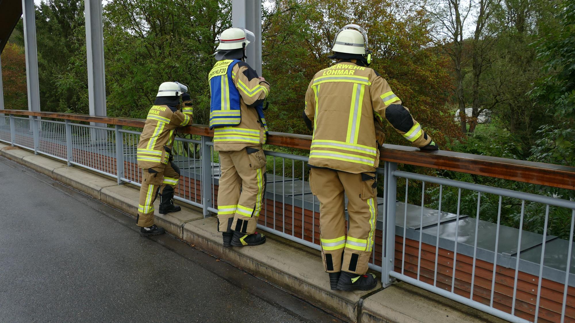 Drei Feuerwehrleute auf einer Brücke schauen ins Wasser.