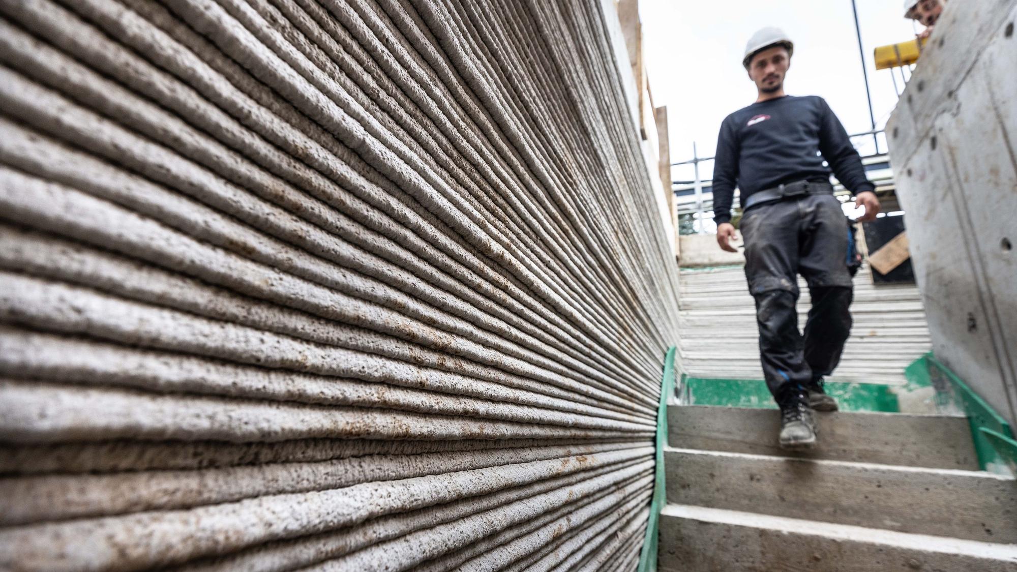 Ein Arbeiter geht auf der Baustelle eines Mehrfamilienhaus aus dem 3D-Drucker. Nach Angaben der Landesregierung entsteht Deutschlands erstes öffentlich-gefördertes Mehrfamilienhaus aus dem 3D-Drucker in Lünen. Die innovative Bauweise ermöglicht den reinen Druck in weniger als 100 Stunden. Das Land fördert das Projekt.