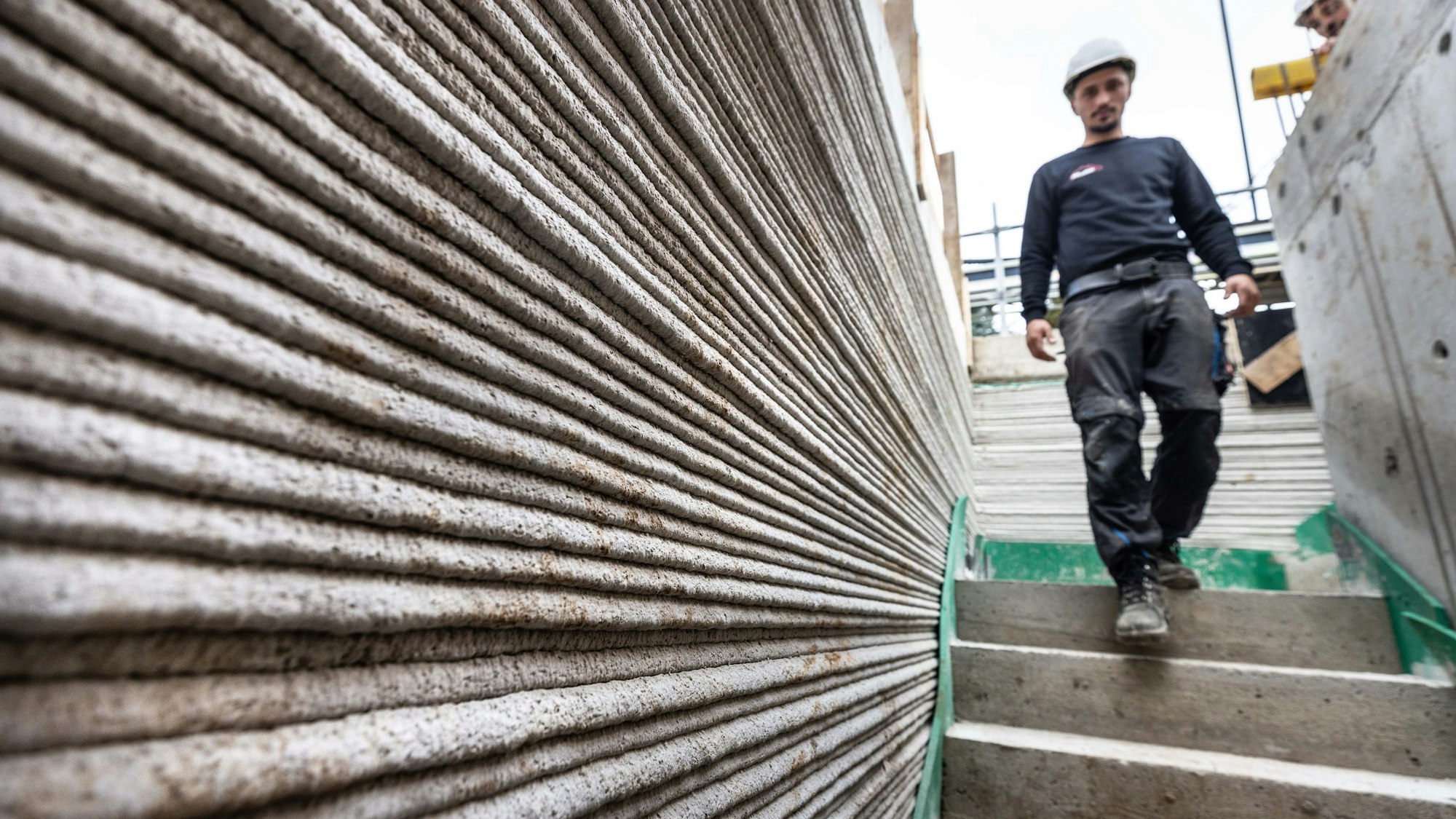 Ein Arbeiter geht auf der Baustelle eines Mehrfamilienhaus aus dem 3D-Drucker. Nach Angaben der Landesregierung entsteht Deutschlands erstes öffentlich-gefördertes Mehrfamilienhaus aus dem 3D-Drucker in Lünen. Die innovative Bauweise ermöglicht den reinen Druck in weniger als 100 Stunden. Das Land fördert das Projekt.