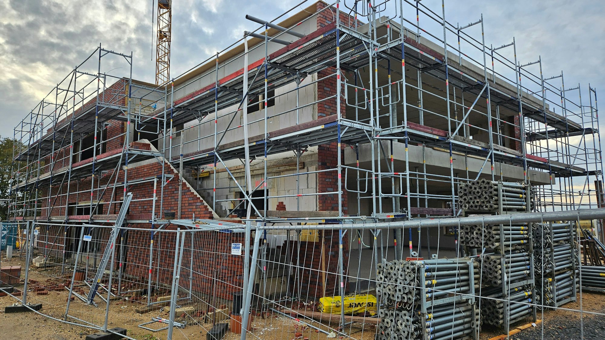 Ein Baugerüst umgibt ein großes, noch nicht fertiggestelltes Gebäude, das von einem Bauzaun geschützt ist.