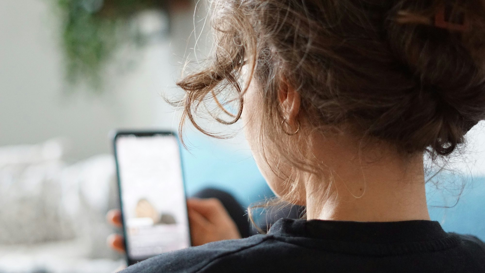 Eine Frau liegt auf einem Sofa und schaut sich ein Video auf der Social-Media-Plattform Instagram auf ihrem Handy an.