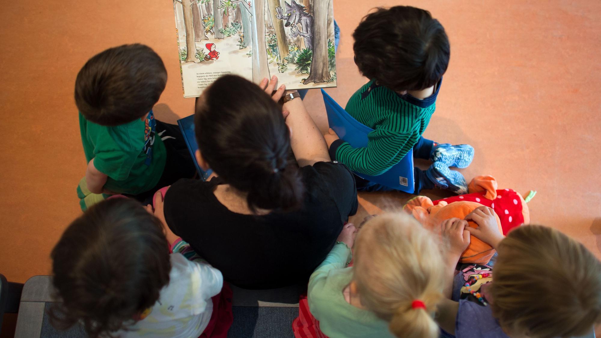 Eine Frau liest mehreren Kindern aus einem Buch vor.