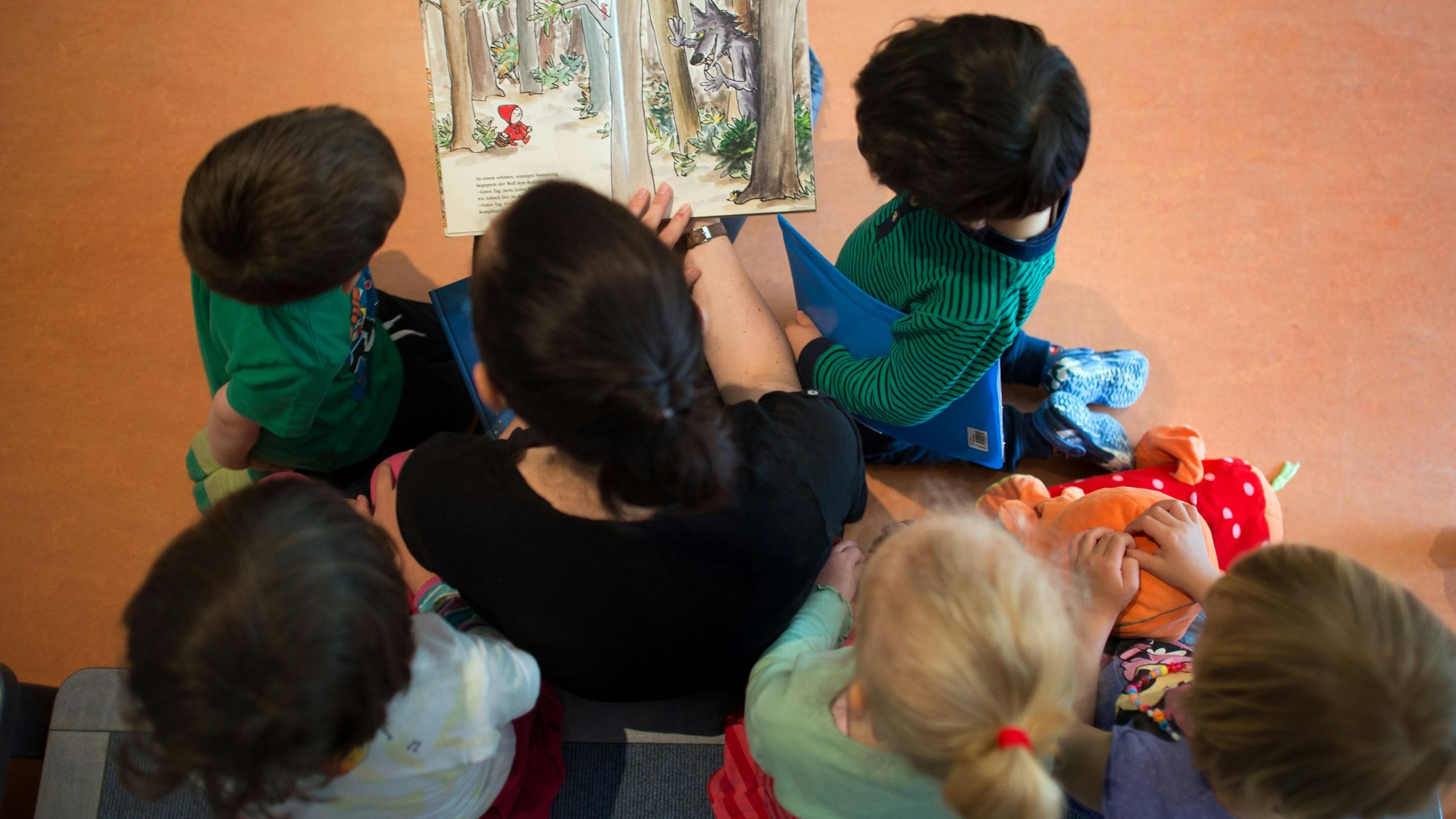 Eine Frau liest mehreren Kindern aus einem Buch vor.