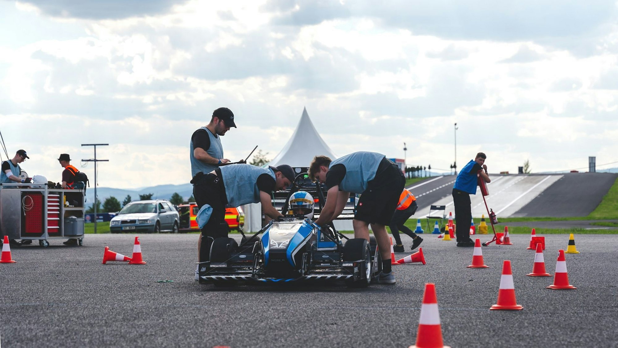Mechaniker des Rennteams aus Sankt Augustin kümmern sich um das blaue Fahrzeug.