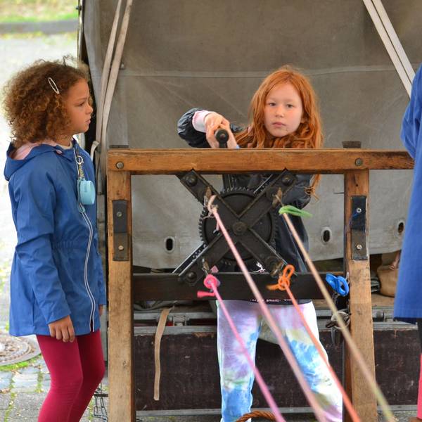 Zwei Mädchen stehen auf dem Handwerkermarkt in Kommern am Stand des Seilers und probieren die alten Geräte aus.