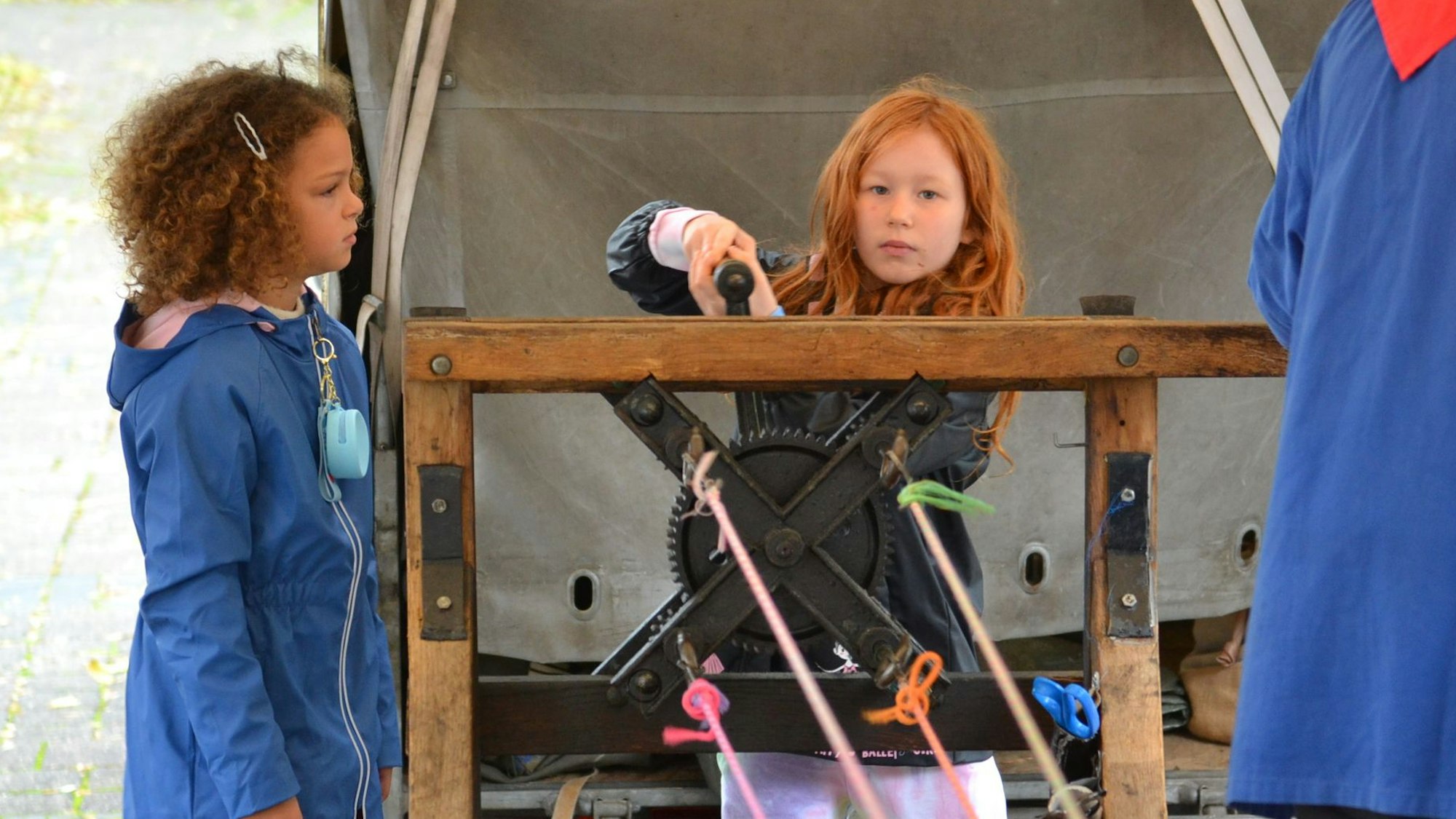 Zwei Mädchen stehen auf dem Handwerkermarkt in Kommern am Stand des Seilers und probieren die alten Geräte aus.