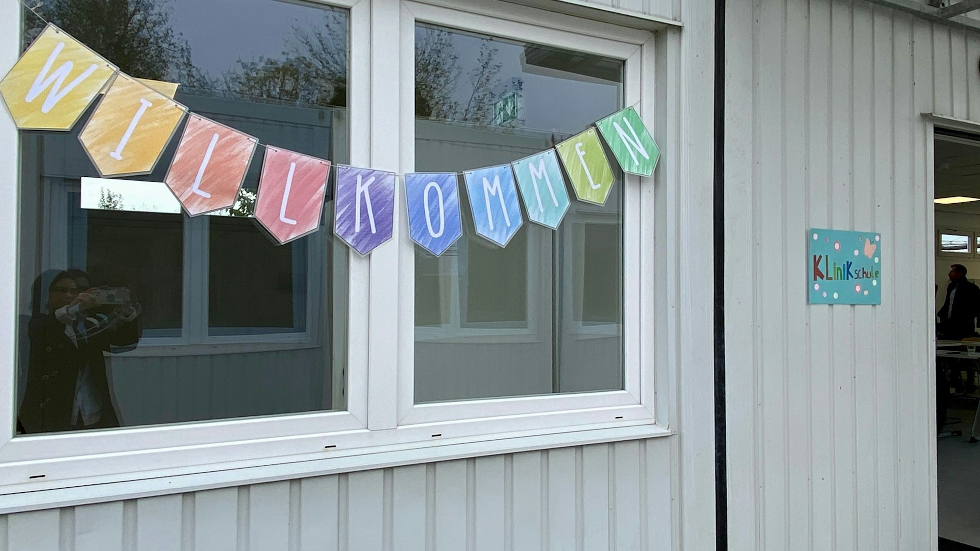 Auf dem Foto ist einer der Container zu sehen, die zu Klassenräumen umfunktioniert worden sind. Vor dem Fenster hängt eine Girlande, auf der „Willkommen“ steht.