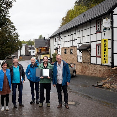 Vier Männer und eine Frau stehen auf einer Straße in Nettersheim an einem Fachwerkhaus. Ein Mann hält eine Mappe mit einer Unterschriftensammlung in der Hand.