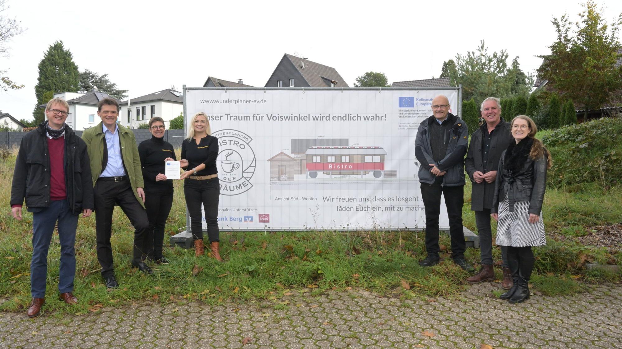 Menschen vor einem Plakat, das einen Zirkuswagen zeigt, der zu einem Café umgebaut werden soll.