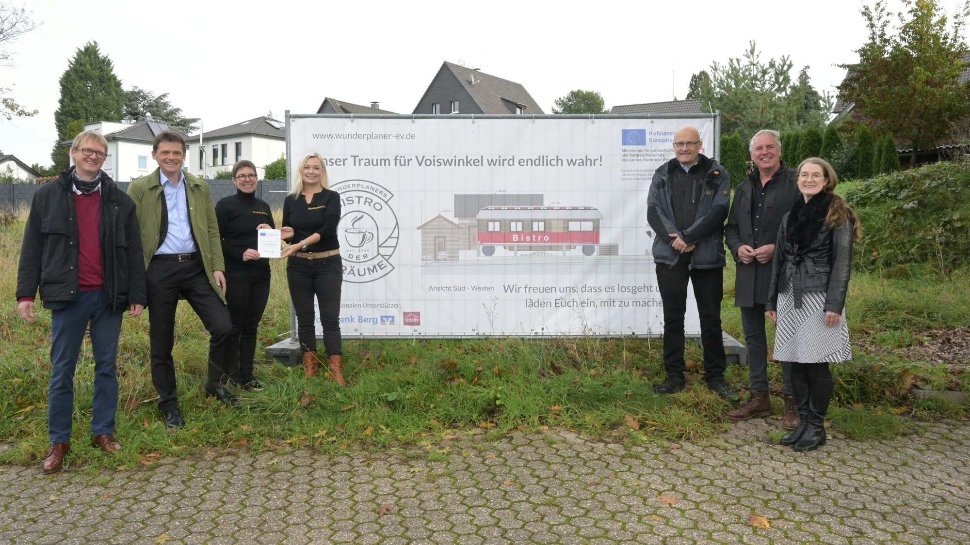 Sieben Männer und Frauen stehen vor einem Wiesengrundstück. Davor ein Plakat mit der Aufschrift: "Unser Traum für Voiswinkel wird endlich wahr!"