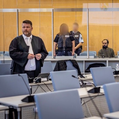 23.10.2023, Nordrhein-Westfalen, Düsseldorf: Der Angeklagte Maan D. (M) wird von Justizbeamten bewacht, er sitzt hinter einer Sicherheitsscheibe auf einem Stuhl. Links steht sein Anwalt Christian Grotenhöfer. ACHTUNG: Justizbeamte wurden auf Anweisung des Gerichts gepixelt +++ dpa-Bildfunk +++