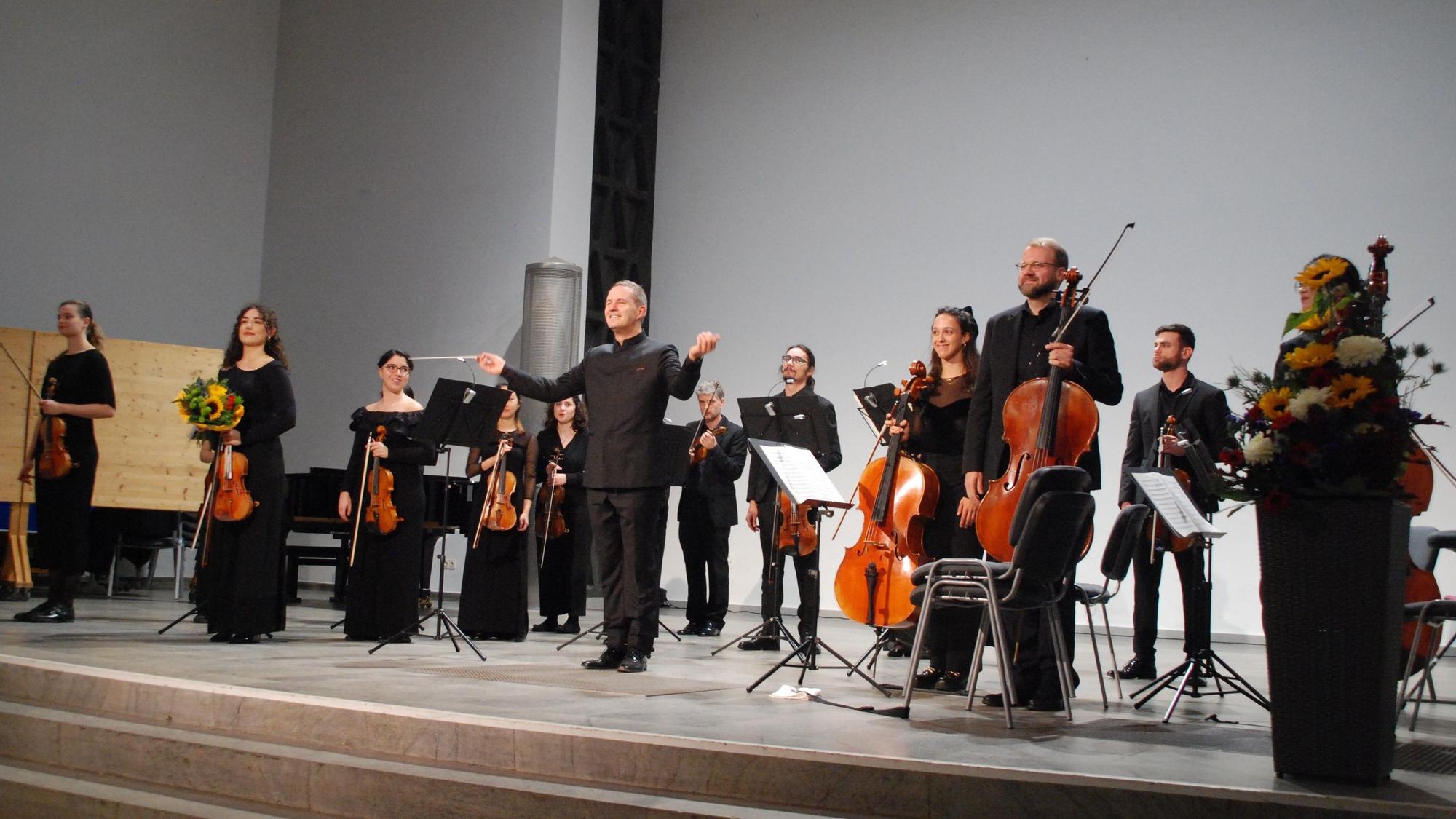 Das Folkwang Kammerorchester Essen unter der Leitung des Dirigenten Johannes Klumpp eröffnet die Spielzeit der Wallgrabenkonzerte. Die Musiker stehen auf der Bühne und halten ihre Instrumente in den Händen.