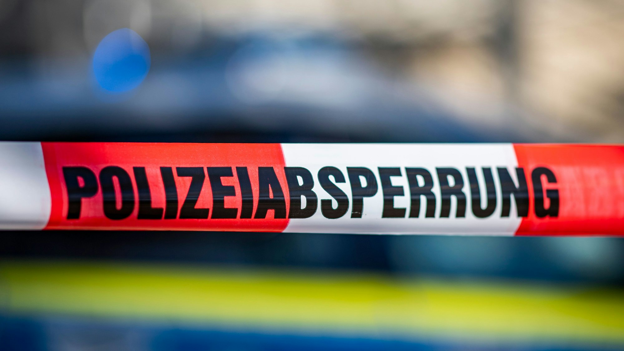 Ein Absperrband mit der Aufschrift „Polizeiabsperrung“ ist vor einem Polizeiwagen aufgespannt.