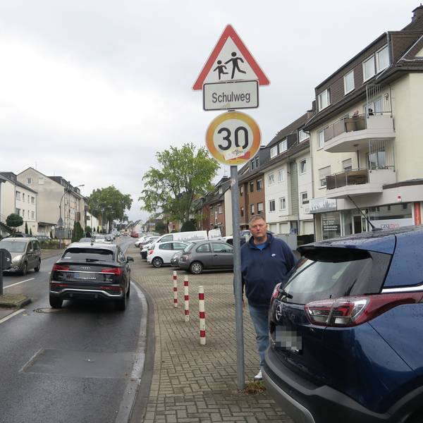 Ein Mann steht an einem Fußgängerüberweg. Autos fahren vorbei und parken am Straßenrand.
