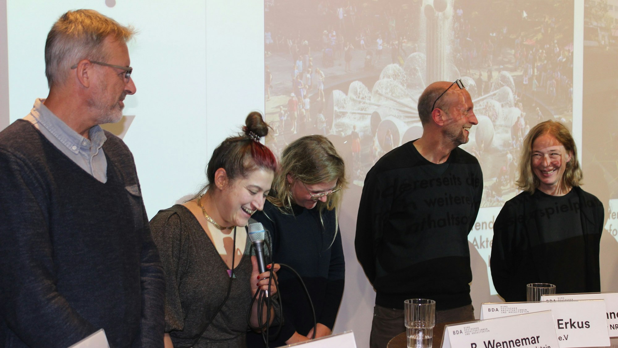 Fünf Menschen stehen vor einer Leinwand auf einem Podium.