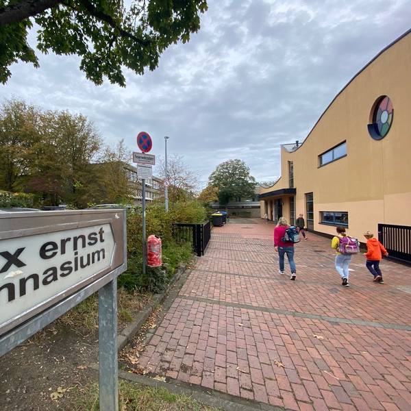 Zu sehen ist im Vordergrund ein Schild, das auf das Gymnasium im Hintergrund hinweist.