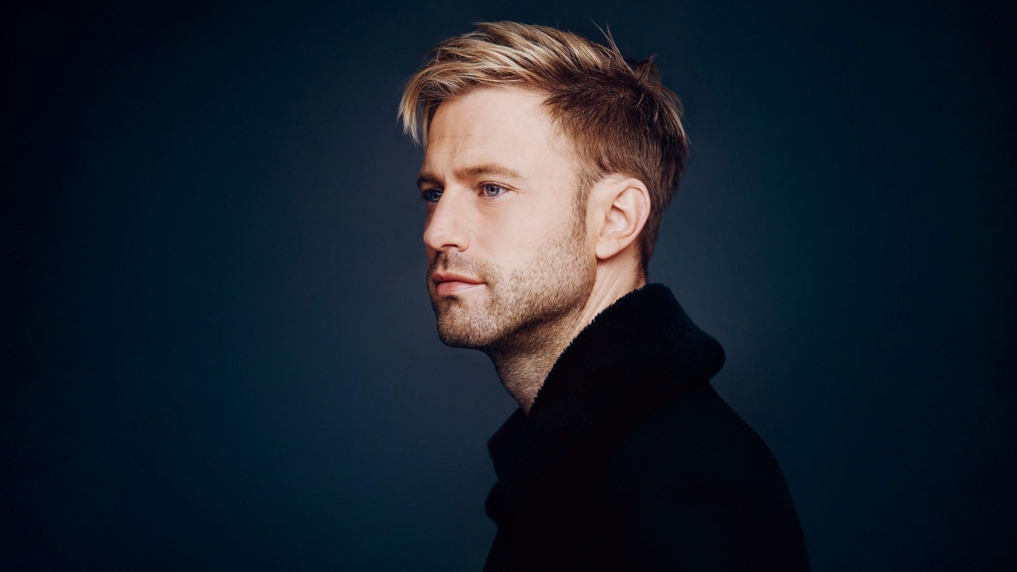 Appl ist auf dem Bild fast im Profil zu sehen, der Hintergrund ist udnkelblau. Er schaut verträumt , hat blondes Haar.