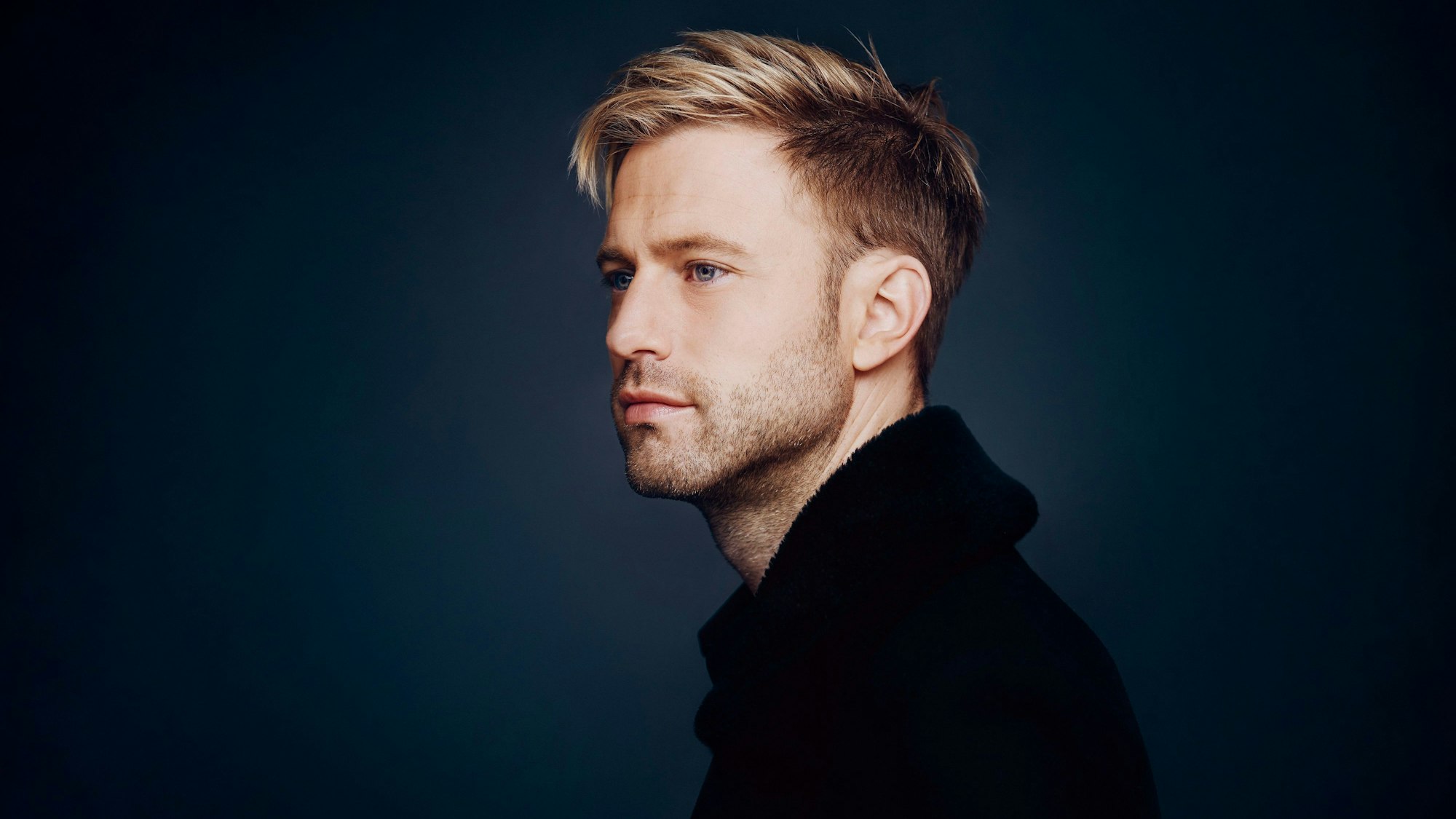 Appl ist auf dem Bild fast im Profil zu sehen, der Hintergrund ist udnkelblau. Er schaut verträumt , hat blondes Haar.
