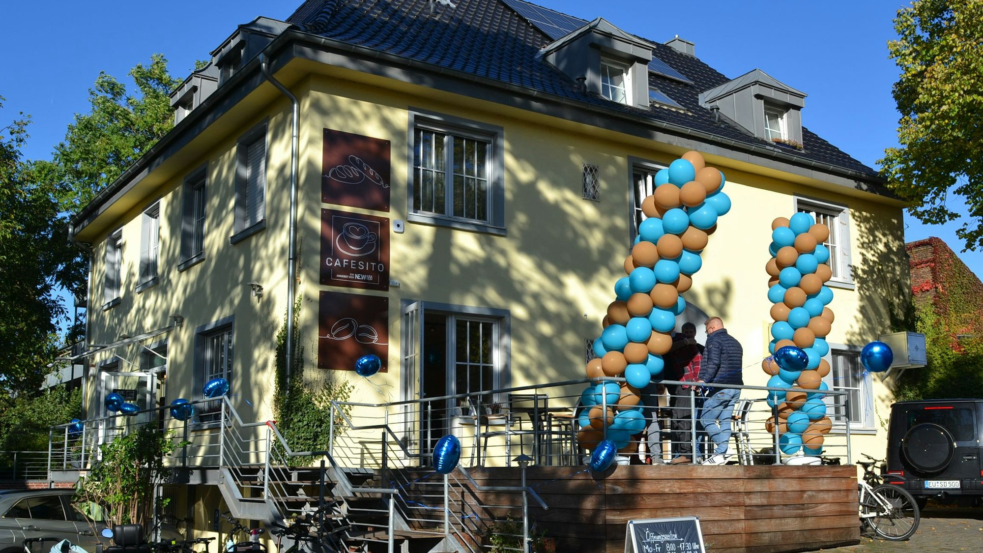 An einem gelben Haus hängen blaue und braune Luftballons.