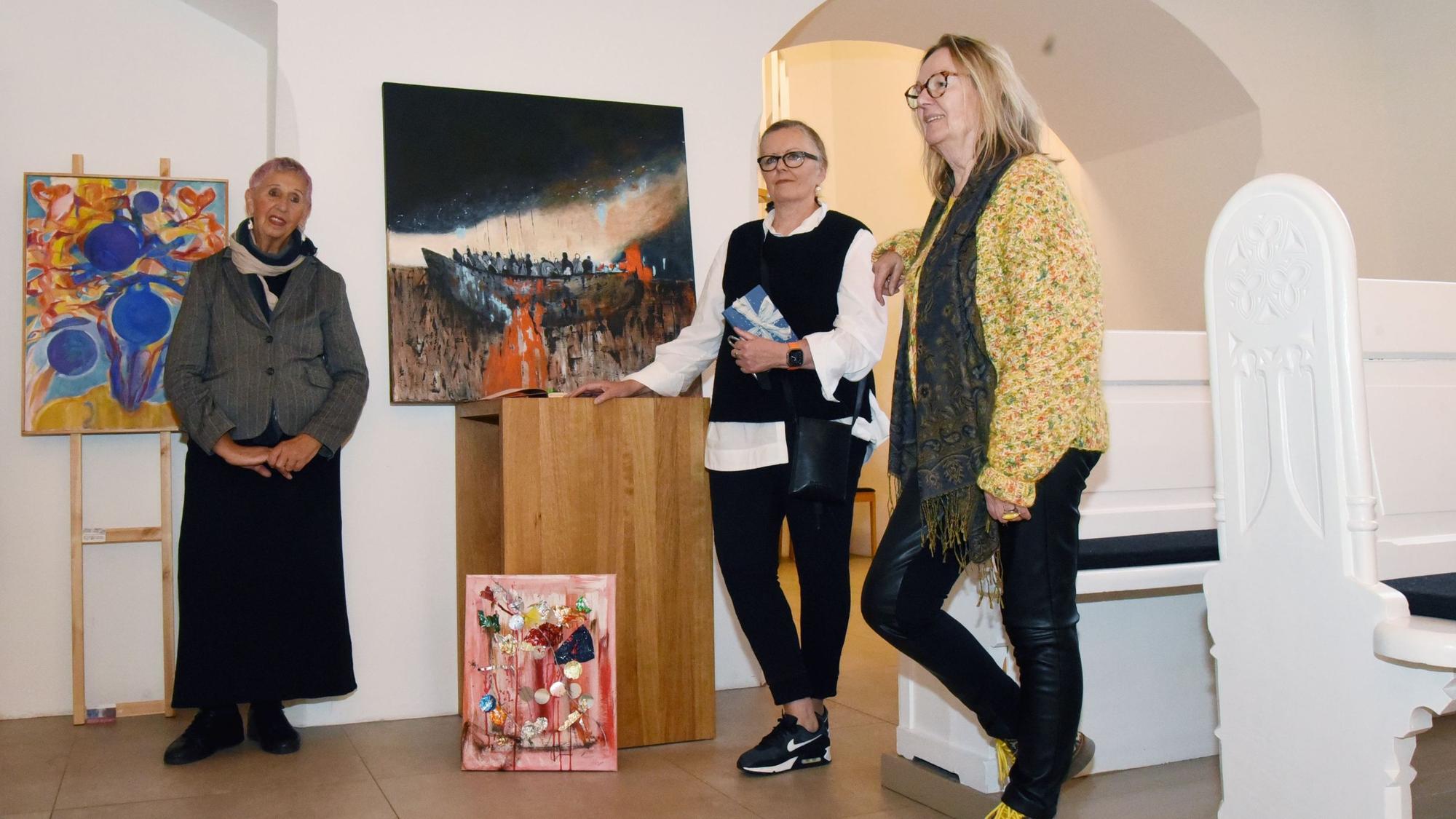 Drei Frauen stehen mit ihren Bildern zwischen Kirchenbänken.