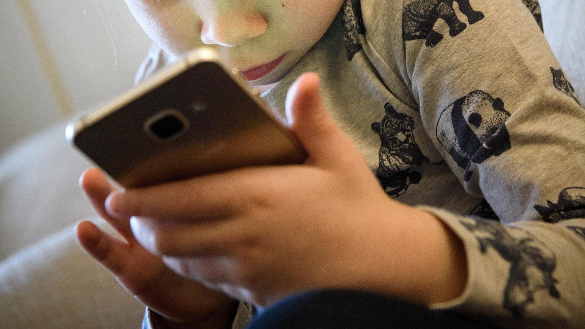 ARCHIV - 08.02.2017, Berlin: Ein kleines Mädchen schaut auf das Display eines Smartphones. Dutzende US-Bundesstaaten ziehen 2023 vor Gericht gegen den Facebook-Konzern Meta mit dem Vorwurf, seine Online-Dienste schadeten Kindern und Jugendlichen. (zu dpa «US-Bundesstaaten in Klage: Facebook und Instagram schaden Kindern») Foto: Hans-Jürgen Wiedl/ZB/dpa +++ dpa-Bildfunk +++