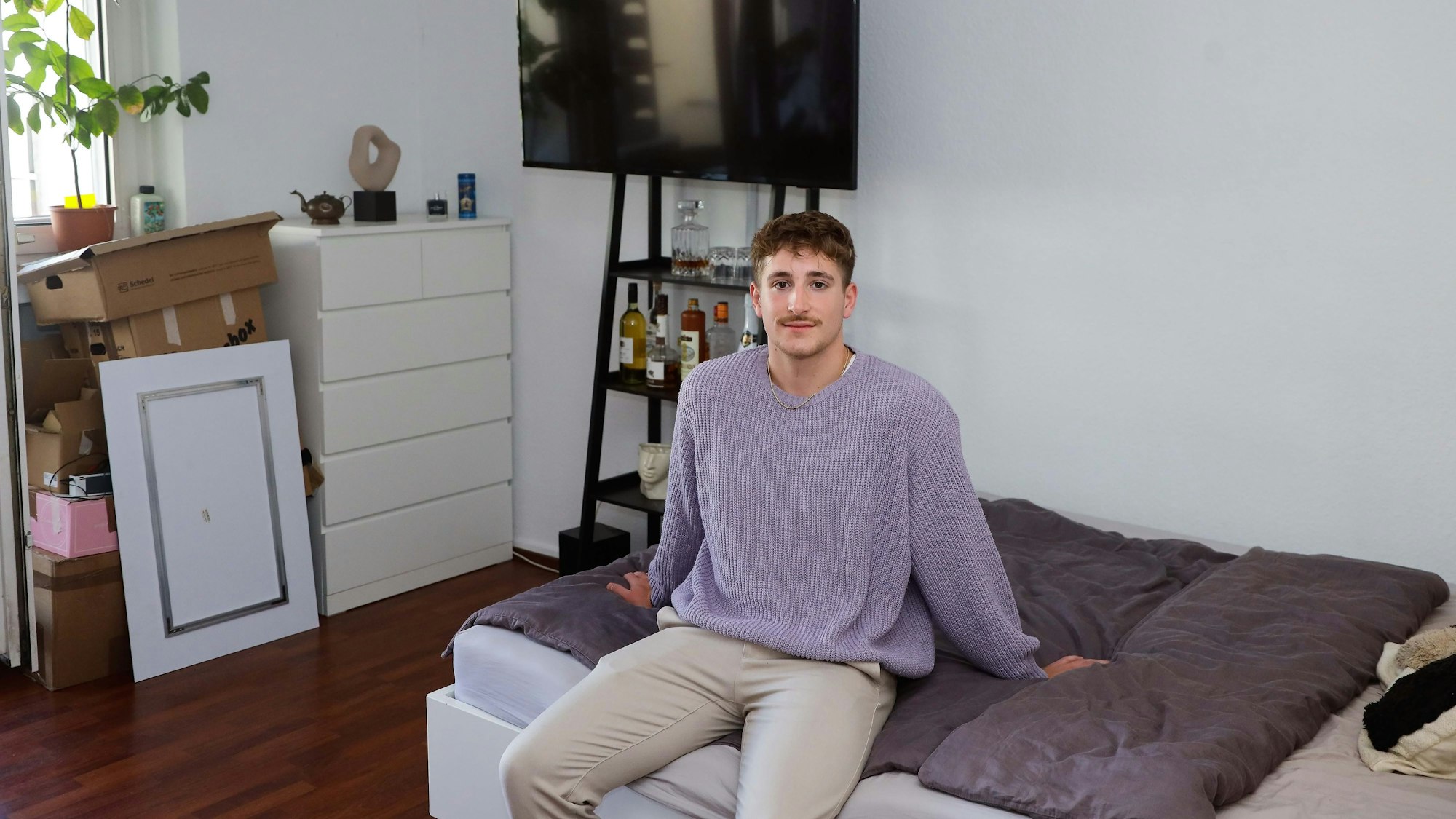 Student Leon sitzt in seinem Kölner WG-Zimmer auf dem Bett.
