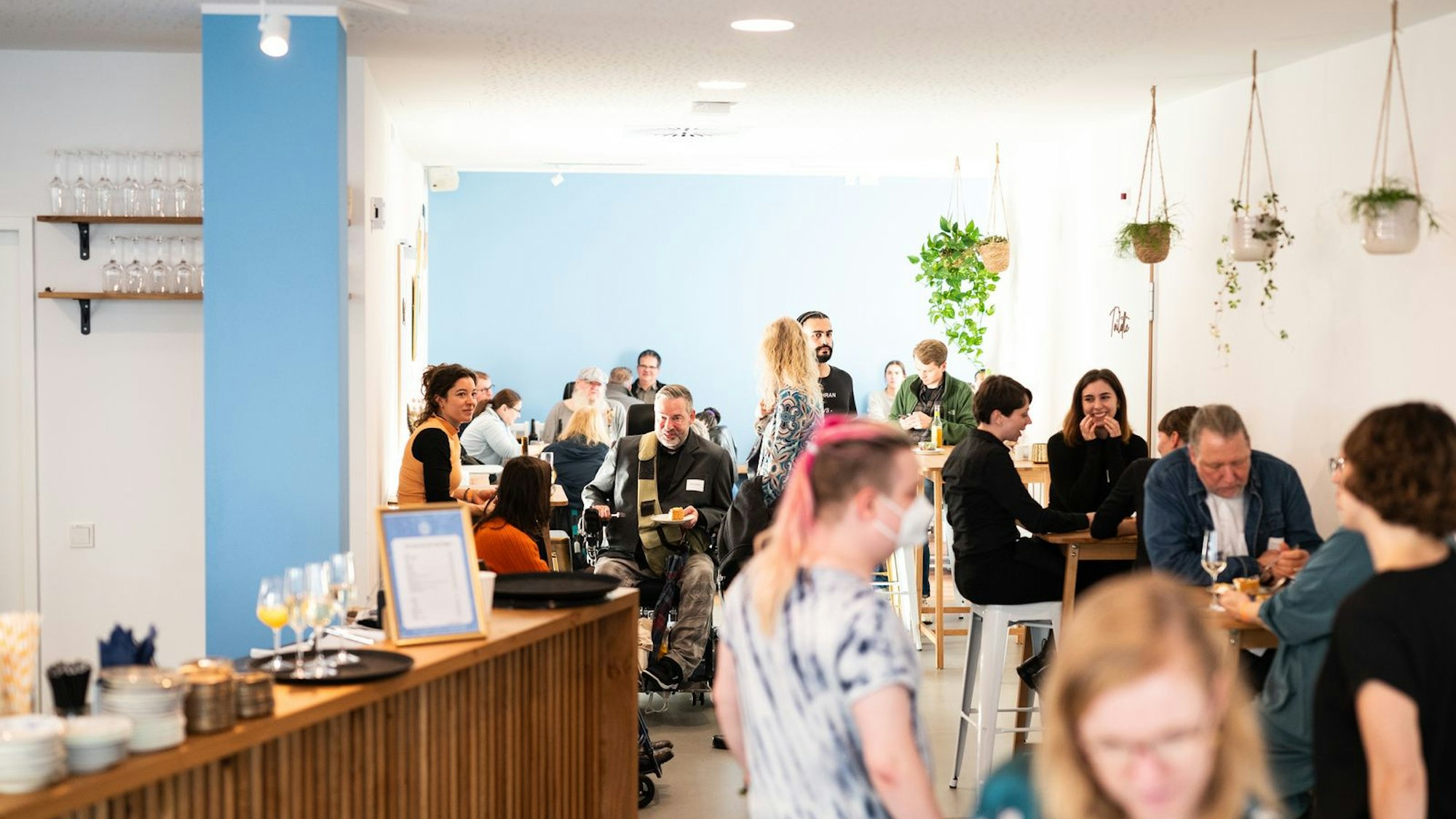 In einem Raum mit Gastro-Theke haben sich viele Menschen mit und ohne Behinderung versammelt.