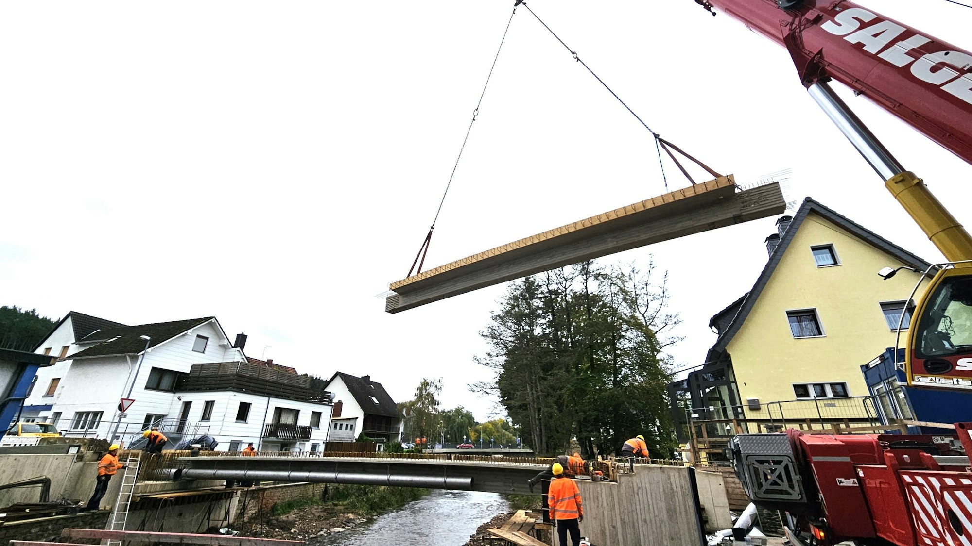Ein Brückenteil hängt an zwei Seilen über der Urft in der Luft.