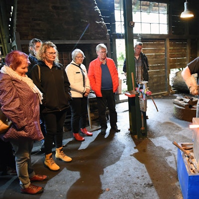 Zwei Männer zeigen vor einigen Besuchern, wie man im Oelchenshammer Eisen schmiedet.