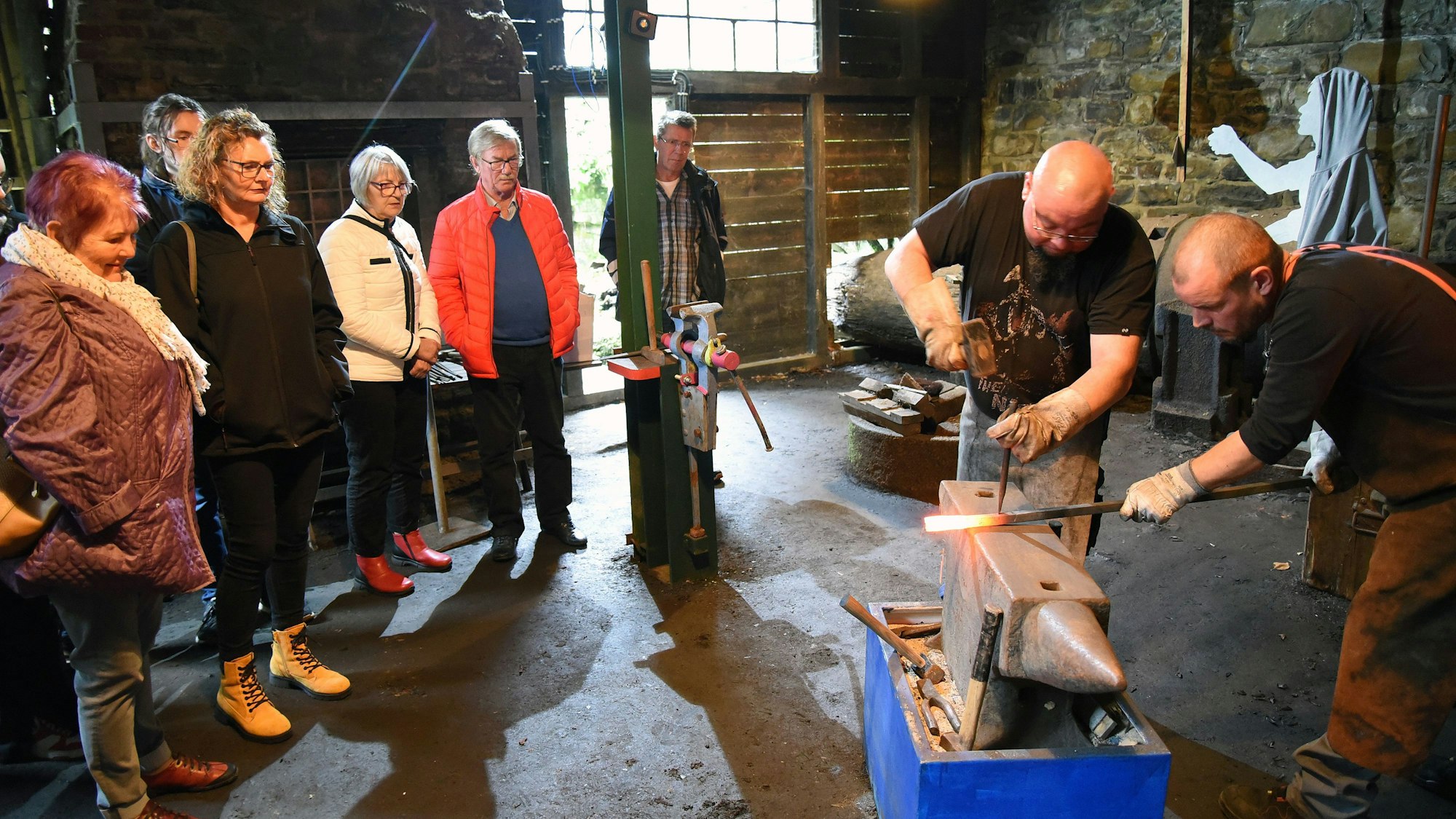 Zwei Männer zeigen vor einigen Besuchern, wie man im Oelchenshammer Eisen schmiedet.