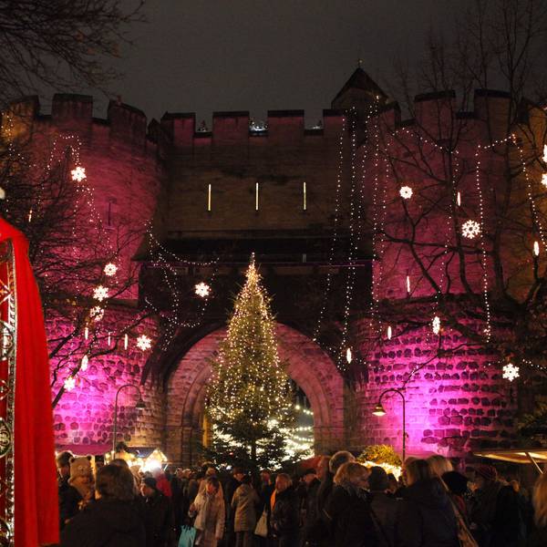 Ein Nikolaus in vollem Ornat steht vor der Kulisse der festlich geschmückten Torburg, ein Weihnachtsmarkt steht unter dem Torbogen.