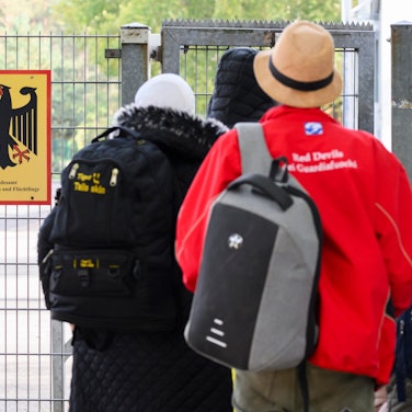 18.10.2023, Niedersachsen, Braunschweig: Geflüchtete betreten neben einem Schild vom Bundesamt für Migration und Flüchtlinge die Landesaufnahmebehörde Niedersachsen am Standort Braunschweig. Die Zahl geflüchteter Menschen, die nach Niedersachsen kommen, wird auf absehbare Zeit nicht sinken. Bei der Unterbringung sind Land und Kommunen an ihre Grenzen gekommen. Ministerpräsident Weil hat am Mittwoch die Landesaufnahmebehörde in Braunschweig besucht. Foto: Julian Stratenschulte/dpa +++ dpa-Bildfunk +++