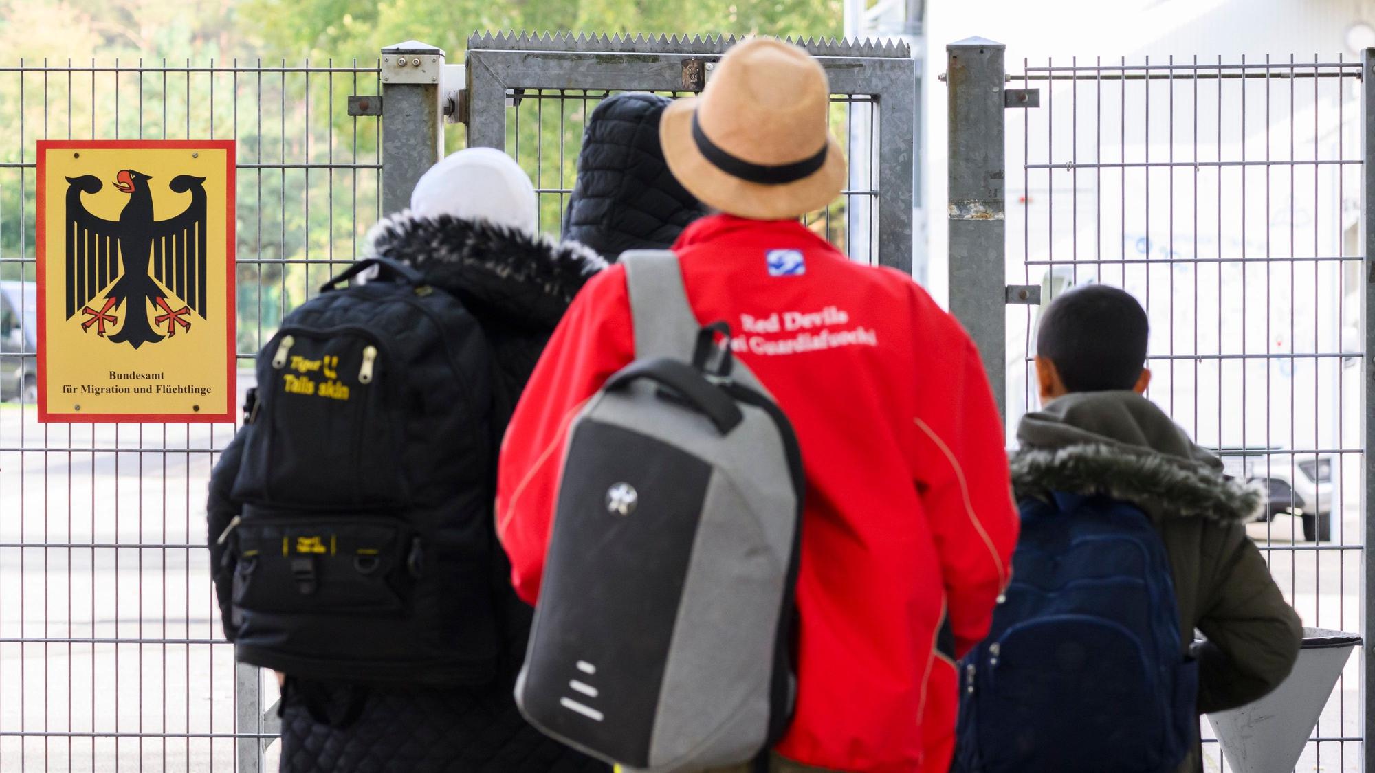 Geflüchtete Menschen betreten neben einem Schild vom Bundesamt für Migration und Flüchtlinge eine Landesaufnahmebehörde. Foto: dpa