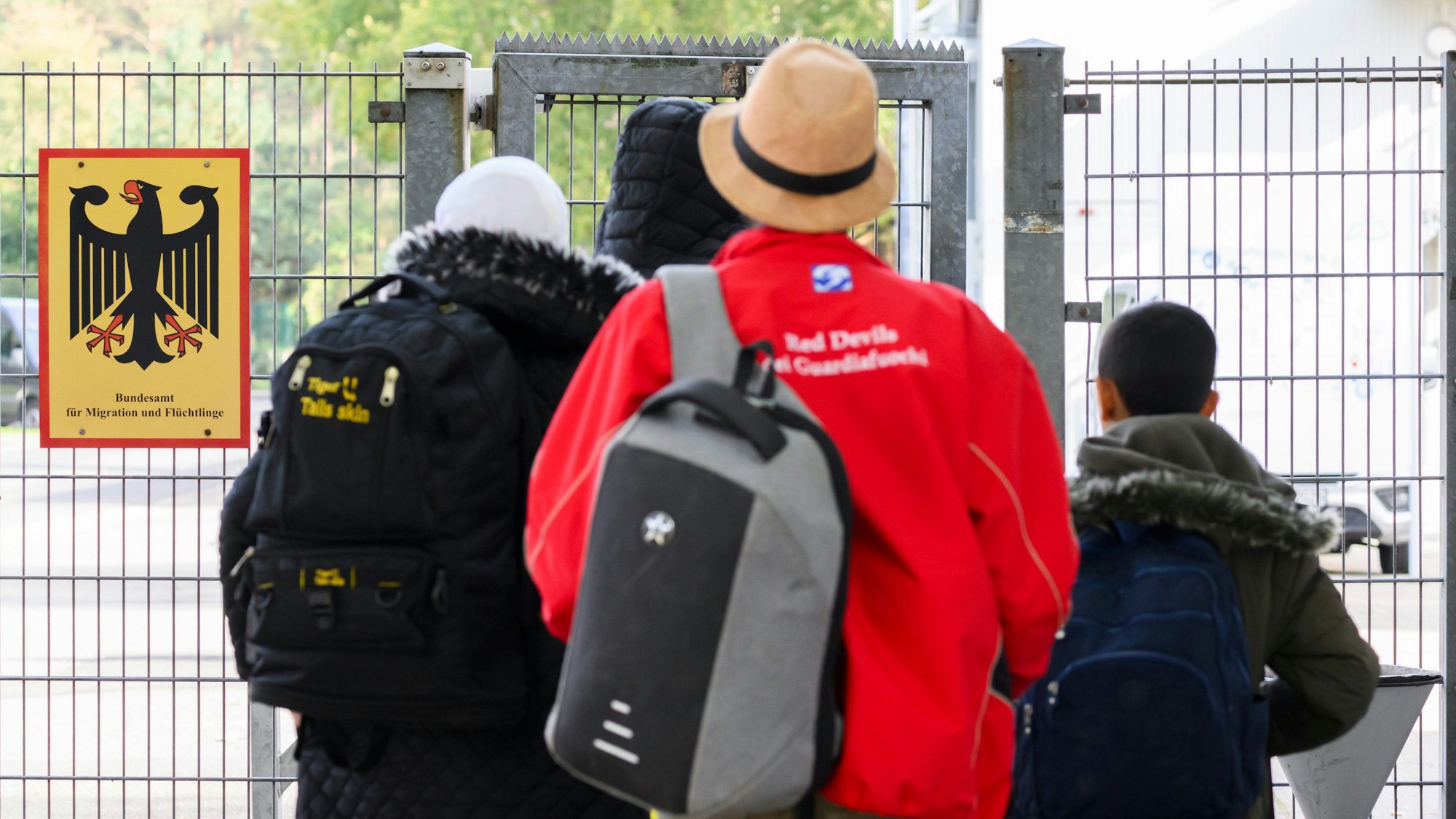 Geflüchtete Menschen betreten neben einem Schild vom Bundesamt für Migration und Flüchtlinge eine Landesaufnahmebehörde. Foto: dpa