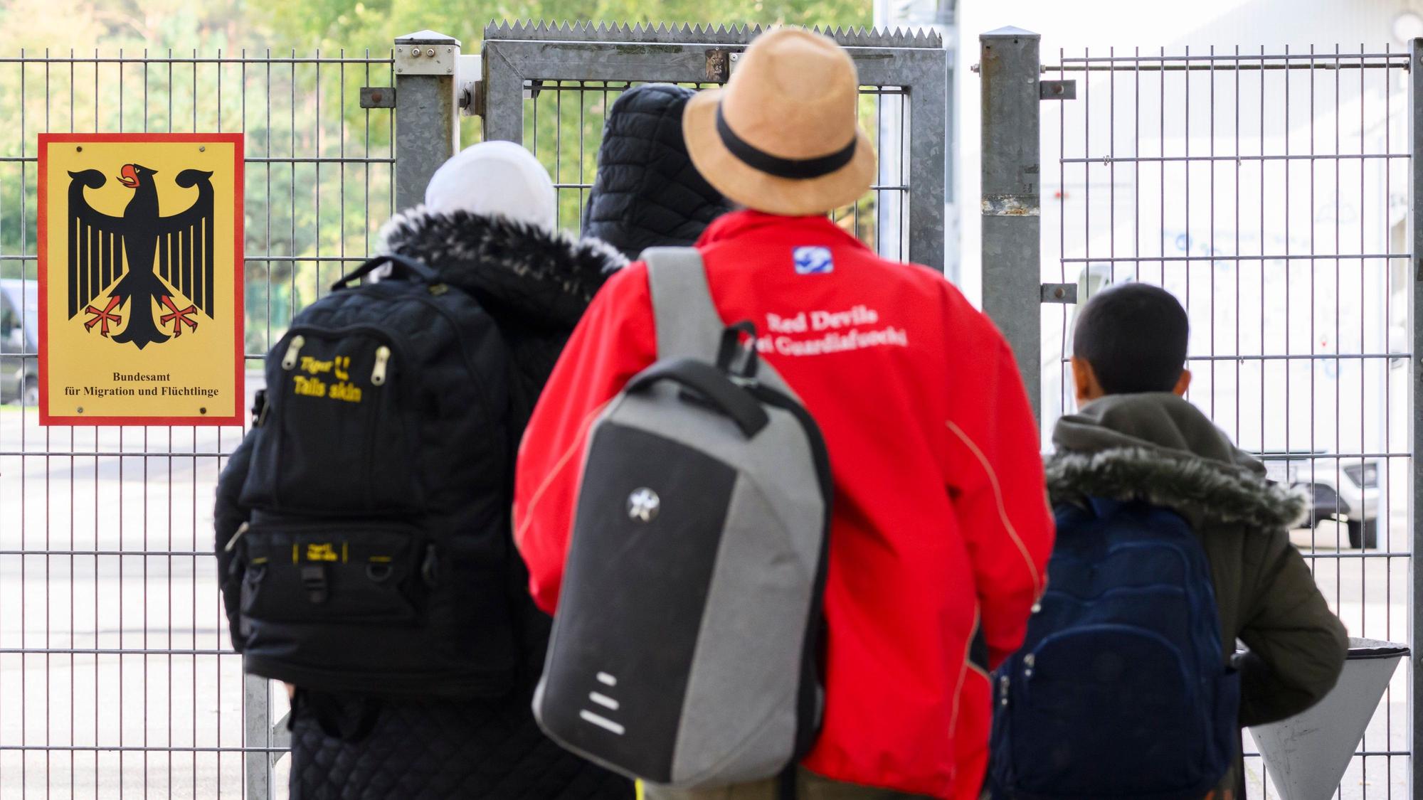 18.10.2023, Niedersachsen, Braunschweig: Geflüchtete betreten neben einem Schild vom Bundesamt für Migration und Flüchtlinge die Landesaufnahmebehörde Niedersachsen am Standort Braunschweig. Die Zahl geflüchteter Menschen, die nach Niedersachsen kommen, wird auf absehbare Zeit nicht sinken. Bei der Unterbringung sind Land und Kommunen an ihre Grenzen gekommen. Ministerpräsident Weil hat am Mittwoch die Landesaufnahmebehörde in Braunschweig besucht. Foto: Julian Stratenschulte/dpa +++ dpa-Bildfunk +++