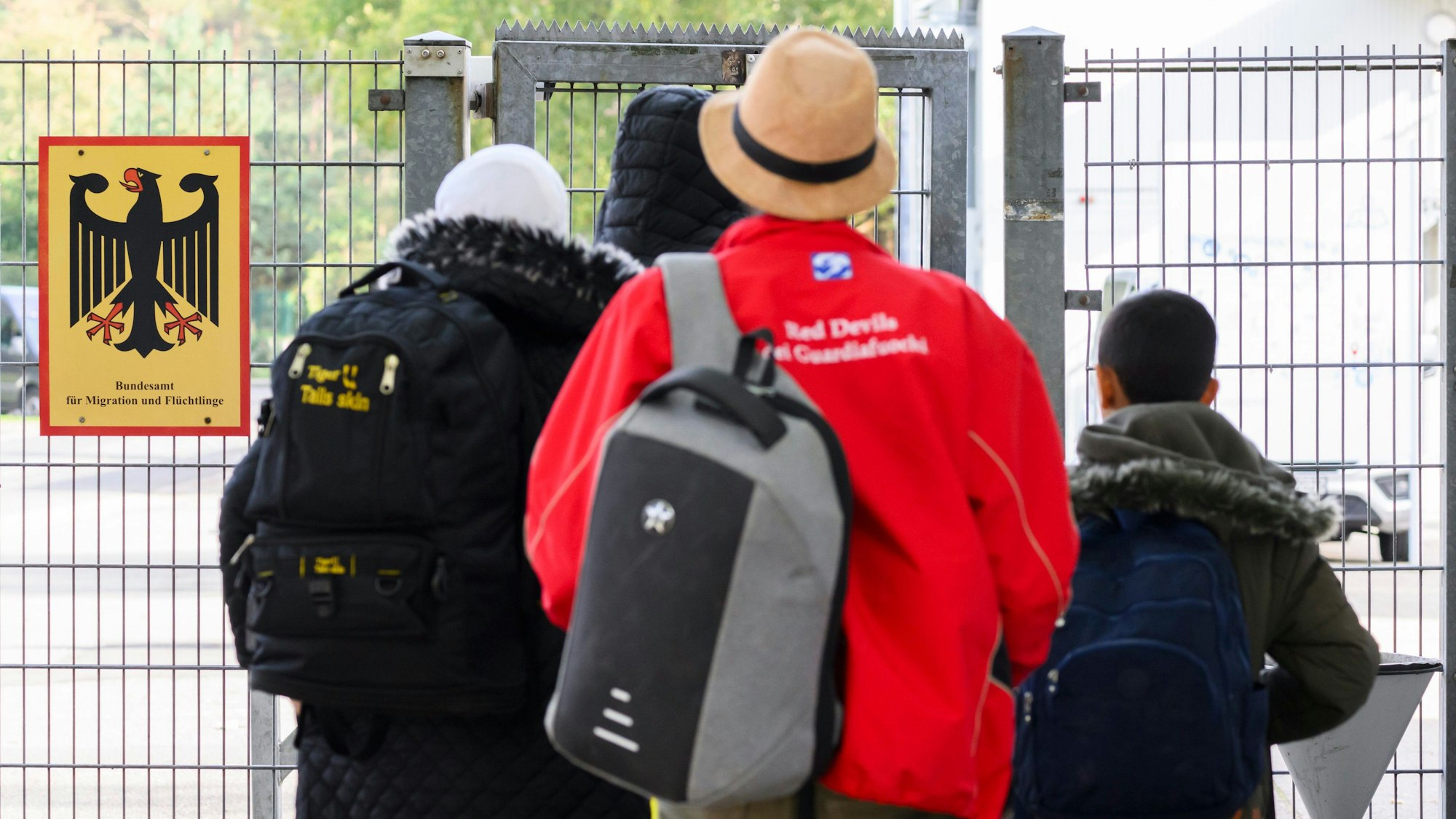 18.10.2023, Niedersachsen, Braunschweig: Geflüchtete betreten neben einem Schild vom Bundesamt für Migration und Flüchtlinge die Landesaufnahmebehörde Niedersachsen am Standort Braunschweig. Die Zahl geflüchteter Menschen, die nach Niedersachsen kommen, wird auf absehbare Zeit nicht sinken. Bei der Unterbringung sind Land und Kommunen an ihre Grenzen gekommen. Ministerpräsident Weil hat am Mittwoch die Landesaufnahmebehörde in Braunschweig besucht. Foto: Julian Stratenschulte/dpa +++ dpa-Bildfunk +++