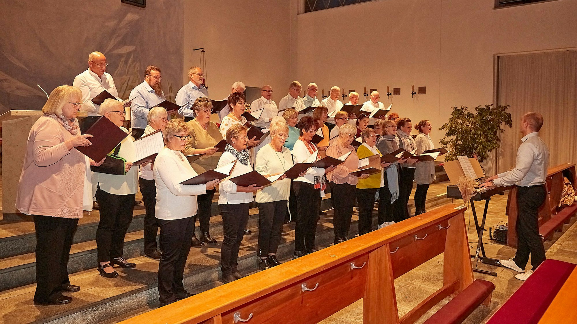 Der Hellenthaler Kirchenchor singt im Altarraum der Kirche. Rechts am Keyboard musiziert Dirigent Christopher Schneider.