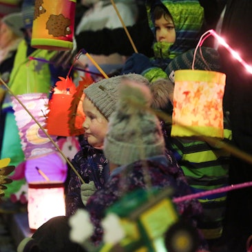Kinder ziehen am mit ihren leuchtenden Laternen bei einem St. Martins-Umzug durch die Straßen.
